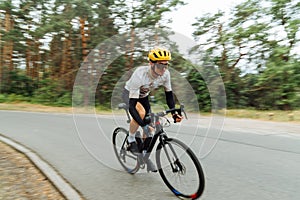 Photo of a professional cyclist riding fast on an asphalt road in the woods