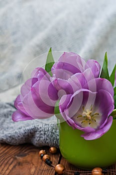 Photo of purple tulip buds in a green mug on a wooden table close-up with a background of light fabric