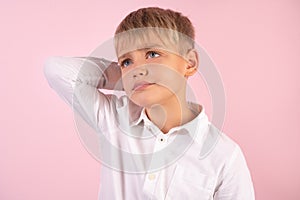 Photo of puzzled boy with stubble, scratches head, looks in bewilderment, dressed in casual white shirt, models against pink