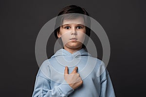 Photo of puzzled boy 10-12 years old pointing finger at herself. Studio shot, gray background. Facial expression concept
