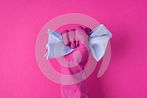 Photo of raised hand in pink glove clenching blue rag into fist on isolated pink background with blank space