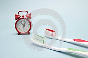 A photo of the red alarm clock and two toothbrushes. Time to clean the teeth. Dental care, personal hygiene concept photo. An impo