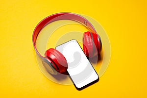 Photo of red headphones with smartphone with white screen in middle over yellow background