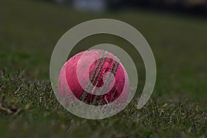 Photo of a red leather cricket ball with stitched seams on grass, cricket ball on green grass pitch with copy space, Close up Cric