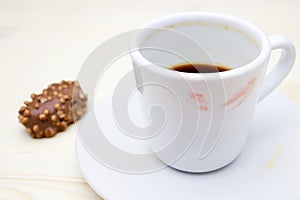 A photo of the red lipstick marks on your coffee cup. Dirty empty white porcelain cup on the plate and a chocolate candy. Messthet