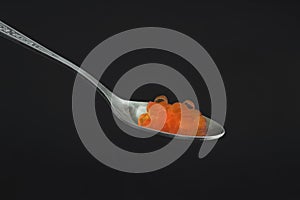 A photo red salmon caviar in an old vintage silver spoon on the dark background. Copyspace, place for text. Delicatessen and