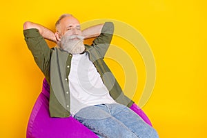 Photo of relaxed dreamy man sit beanbag hold hands behind head wear green shirt isolated yellow color background