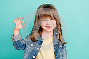 Photo of reliable little girl show okey sign approve choice wear jeans jacket  aquamarine color background