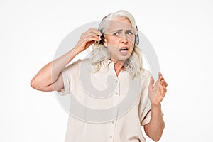 Photo of retired female pensioner with gray hair putting off wireless earphones while listening to music and trying to