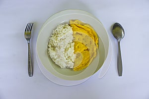 a photo rice with fried egg omelet, with spoon and fork on white plate. isolated on wood background. breakfast with omelet in.