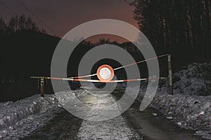 Photo of road barrier with no vehicles sign on the road at night. Gate barrier on the forest road in winter