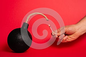 Photo of a round bomb with lit fuse on a red background. Big bomb on red background. Vertical