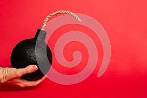 Photo of a round bomb with lit fuse on a red background. Big bomb on red background. Vertical