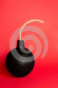 Photo of a round bomb with lit fuse on a red background. Big bomb on red background. Vertical