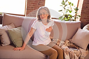 Photo of sad depressed retired woman dressed white t-shirt sitting couch having heart pain arm hand chest indoors flat