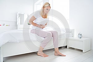 Photo of sad elderly barefoot lady sitting bed linen morning suffer painful periods feel bad menopause concept room