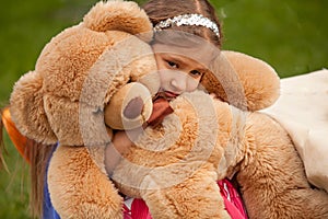 Photo of sad little girl hugging teddy bear