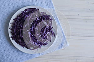 Photo salad of chopped purple cabbage in a plate on a blue napkin on a light background.