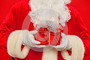 Photo of Santa Claus gloved hand with giftbox, on a red background. Christmas