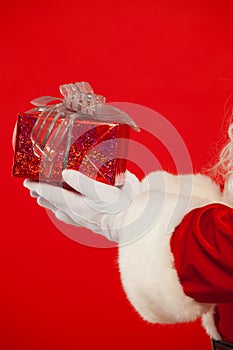 Photo of Santa Claus gloved hand with giftbox, on a red background. Christmas