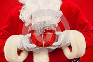 Photo of Santa Claus gloved hand with giftbox, on a red background. Christmas