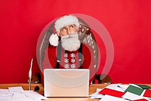 Photo of santa claus think dream look empty space sit table use laptop north-pole eve isolated over red color background