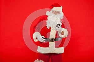 Photo of Santa Claus using mobile phone, on a red background. Ch