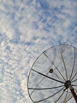 Photo of a satellite dish with a blue sky background filled with white clouds