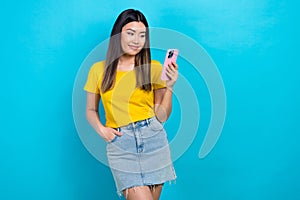 Photo of satisfied girl dressed yellow t-shirt look at smartphone facebook twitter instagram whatsapp isolated on blue