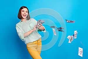 Photo of satisfied gorgeous woman with bob hairstyle dressed teal shirt get rich throw flying money isolated on blue