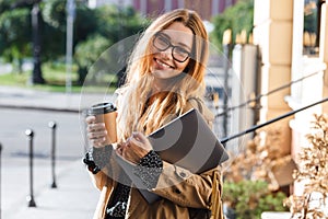 Photo of satisfied woman 20s holding laptop while walking through city street