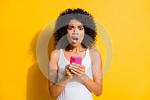 Photo of scared amazed brunette afro american woman hold phone wear white tank-top isolated on yellow color background