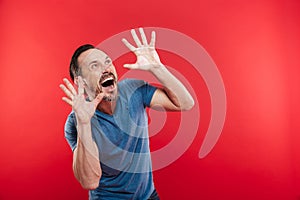 Photo of scared man with beard and mustache shouting and gesturing with hands while looking upward on copyspace, isolated over re