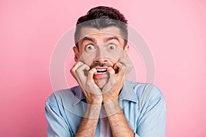 Photo of scared shocked young man bite nails hold hands mouth isolated on pastel pink color background