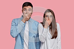 Photo of scared speechless lady and man cover mouthes with palms, have stupefied expressions, dressed in elegant shirt