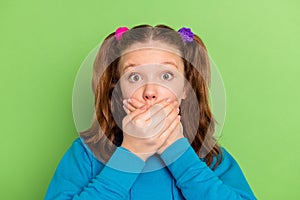 Photo of scared young small girl hold hands face cover mouth tell secret isolated on green color background