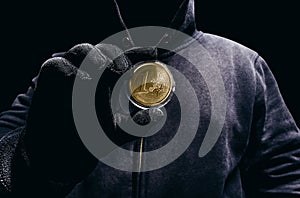 Photo of scary hooded man holding golden euro coin