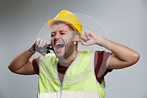 Photo of screaming builder man in yellow helmet with walkie-talkie on empty gray background.