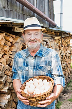 Senior farmer wearing hat while carrying fresh eggs in basket in barn