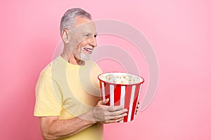 Photo of senior grey hair old man eating tasty bucket crisps looking curious empty space new marvel film isolated on