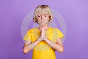 Photo of serious blond kid palms together plead request wear yellow t-shirt  violet color background