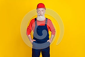 Photo of serious confident age man workwear overall red hard hat arms pockets isolated yellow color background