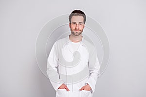 Photo of serious confident young guy doctor workwear standing arms pockets isolated grey color background