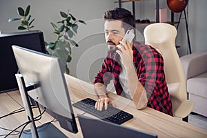 Photo of serious focused young man write computer programmer hold phone talk indoors inside office workplace
