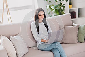 Photo of serious focused young woman sit sofa type message on laptop work form home indoors inside house