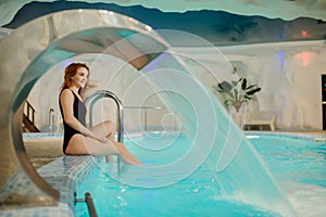 Photo of sexy beautiful reddish woman in black bath costume near the swimming pool of a spa centre