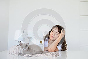 Photo of a sexy brunette working at the sewing machine and playing with a gray kitten