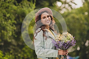 Photo of shiny adorable young woman dressed teal jacket glasses cap getting bunch wildflowers outdoors city park