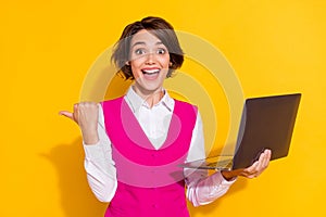 Photo of shiny excited young lady wear pink suit holding modern device pointing thumb empty space smiling isolated