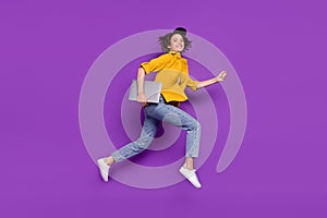 Photo of shiny pretty young woman dressed yellow shirt smiling jumping running holding modern device isolated purple